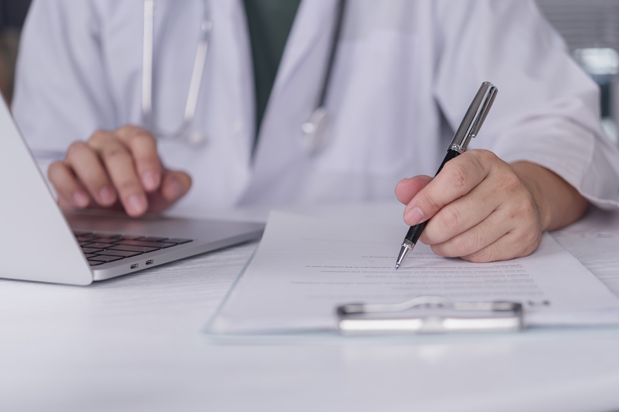Doctor,Hands,Writing,Medical,Report,Clipboard,And,Using,Laptop,At